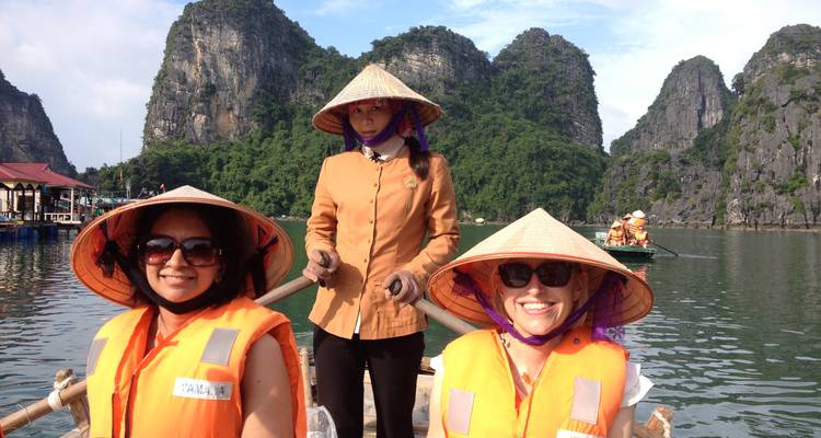 Trois femmes en gilets de sauvetage et chapeaux coniques profitent d'une promenade en petit bateau sur des eaux émeraude entourées de karsts calcaires.