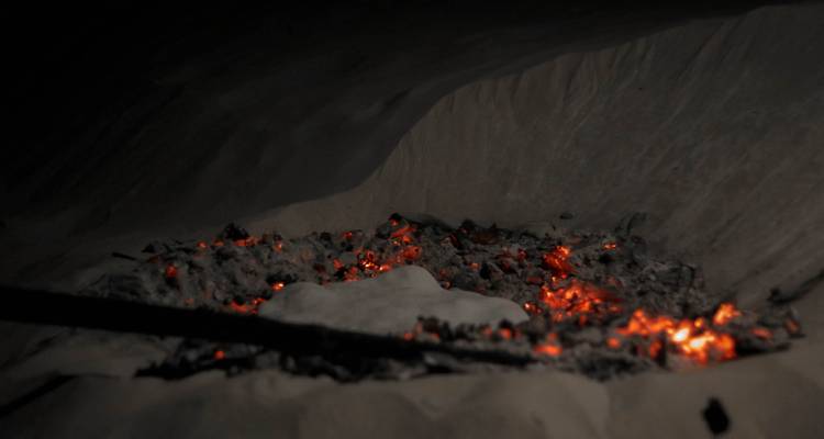Feu de camp avec des braises incandescentes dans le sable.