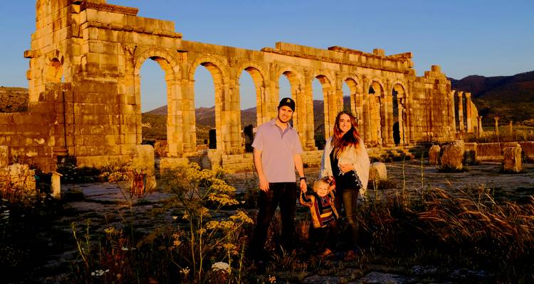 Famille posant devant des ruines antiques au coucher du soleil.