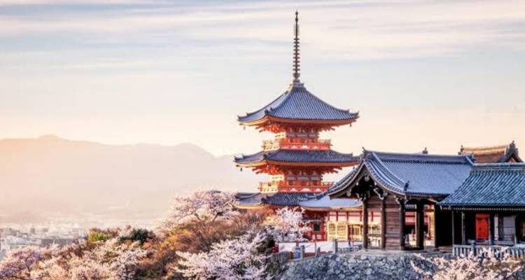 Traditional pagoda of Kiyomizu-dera temple framed by cherry blossoms at sunrise over Kyoto.