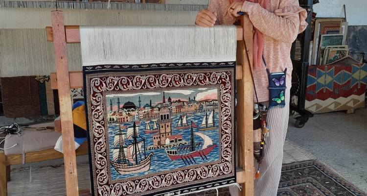 Eine Person, die neben einem detaillierten Wandteppich an einem Webstuhl steht.