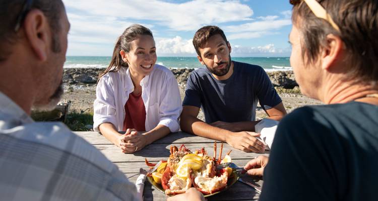 Gruppe von Menschen, die eine Meeresfrüchte-Mahlzeit im Freien am Meer genießen.