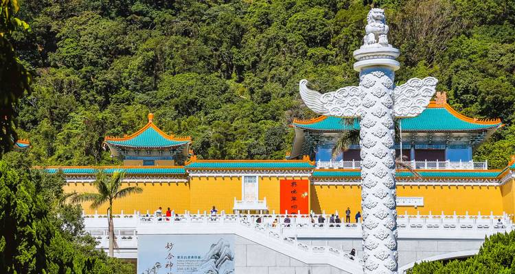 Complexe de palais chinois traditionnel avec des murs jaunes et des toits turquoise situé contre une colline boisée et un pilier ornemental