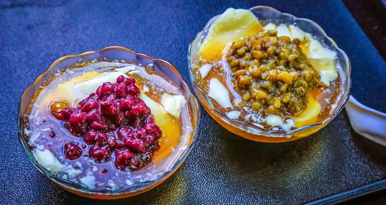 Deux bols en verre de desserts glacés pilés taïwanais colorés garnis de fruits et de haricots sur un plateau sombre