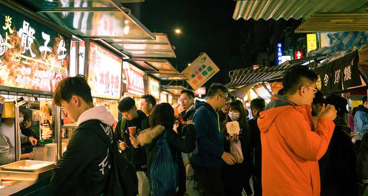 Scène animée de marché nocturne avec des étals de nourriture, des enseignes au néon brillantes et des foules de gens qui mangent et font leurs achats