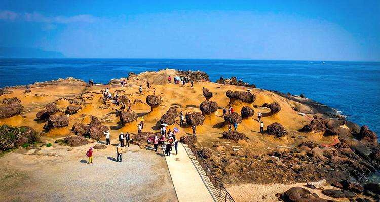 Plateforme côtière rocheuse avec des formations inhabituelles en forme de champignons et des touristes marchant le long d'une promenade en bois sous un ciel bleu