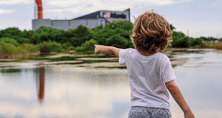 A child pointing towards a building across a reflective pond.