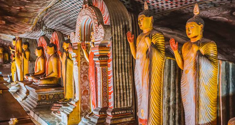 Línea colorida de estatuas de Buda en un pasillo de templo en cueva ricamente pintado.