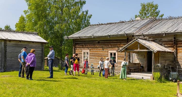 Gruppe von Menschen vor einem traditionellen Holzhaus.