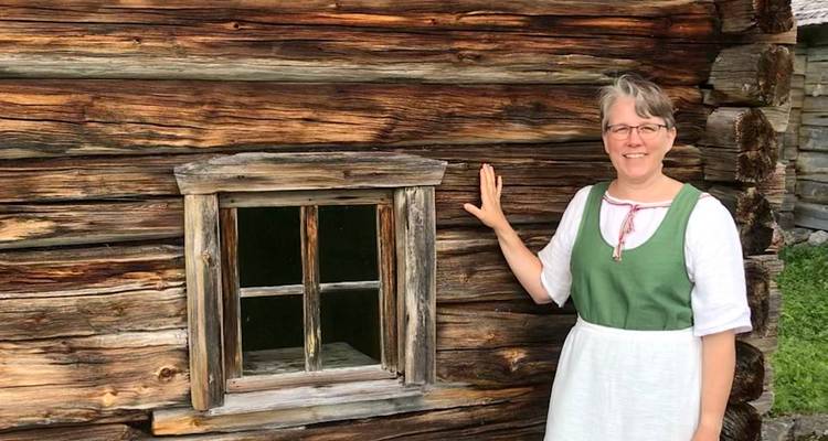 Frau, die an einer Holzhauswand steht.