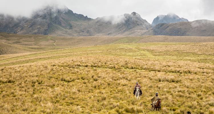Zwei Menschen zu Pferd reiten durch eine malerische Berglandschaft.