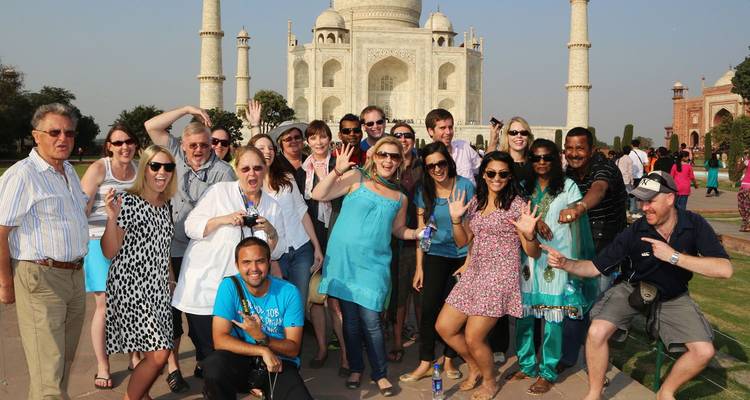 Un grupo de turistas alegres posa saludando frente al Taj Mahal de mármol blanco en un día soleado