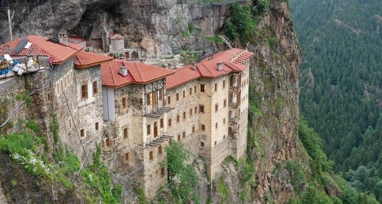 Sumela Monastery built into the side of a cliff with lush forest.