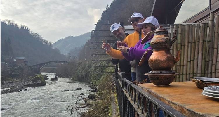 People enjoying tea on a balcony with river and bridge view.