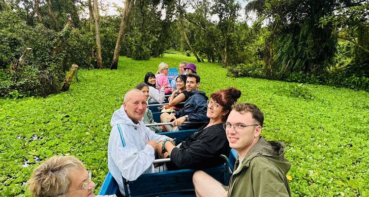 Touristen fahren in einem offenen Boot durch ein enges Mekong-Seitenwassergebiet, das mit schwimmender Vegetation bedeckt ist.