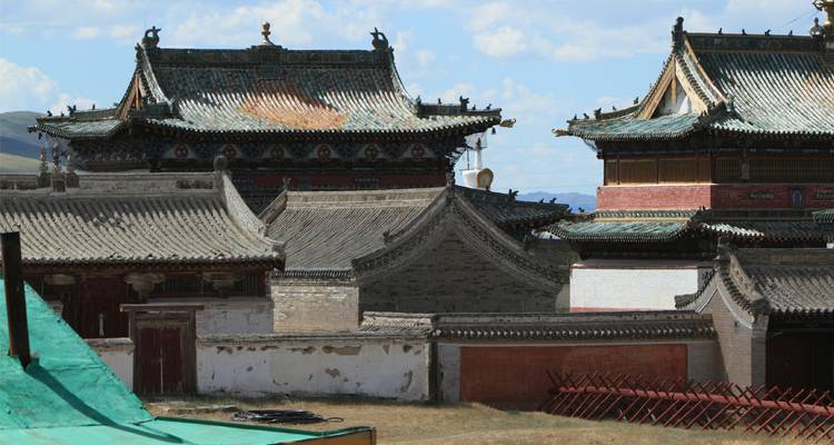 Ancient tiled roofs and ornate temples of the Erdene Zuu Monastery complex under blue sky.