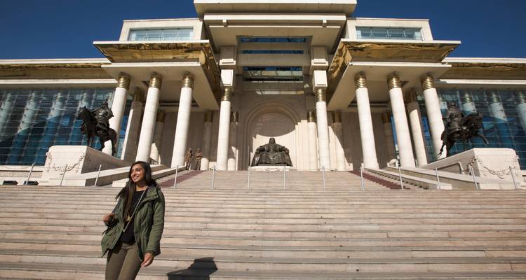 Traveller poses on the steps leading to the Government Palace and Genghis Khan statue on a clear day.