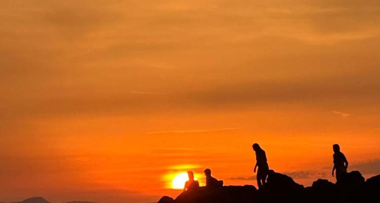 Silueta de personas observando el atardecer sobre terreno rocoso.
