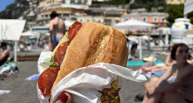 Primer plano de un sándwich sostenido con la playa de fondo.
