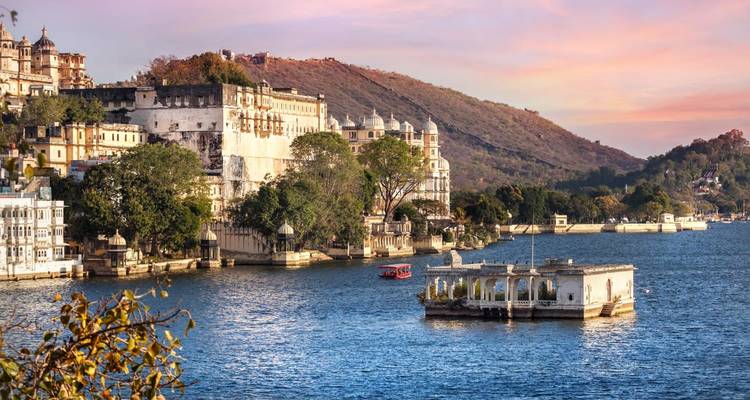Stadtgebäude an einem See mit Hügeln im Hintergrund bei Sonnenuntergang.