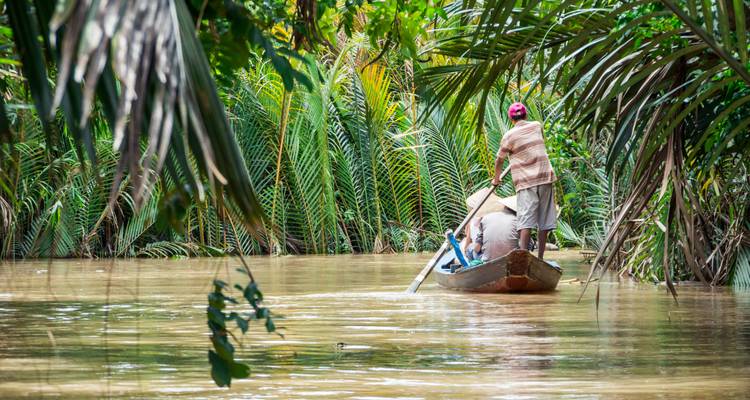 Mensen die een boot peddelend door een weelderige waterweg met dichte groene vegetatie varen.