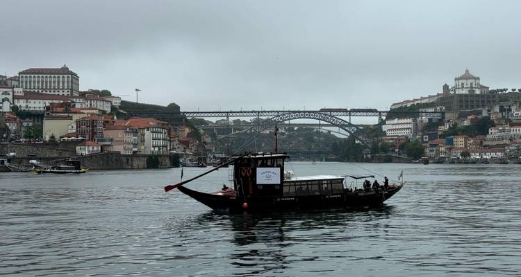 A boat sailing near the Dom Luís I Bridge in Porto on a cloudy day.