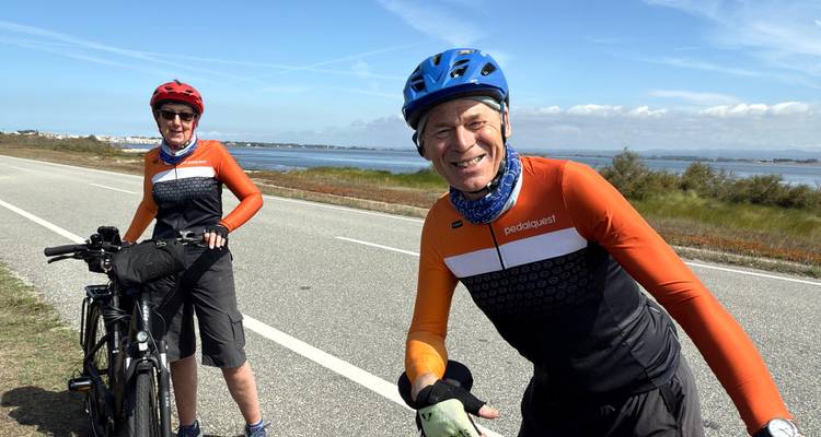 Two cyclists posing on a road with the ocean in the background.