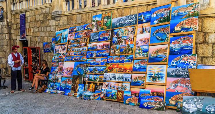 Straatkunstkraam met levendige schilderijen van Adriatische taferelen tegen de stenen muren van Dubrovnik.