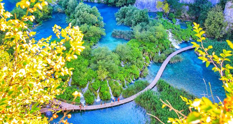 Luchtfoto van een slingerende houten loopbrug over smaragdgroene meren en watervallen in weelderig groen.