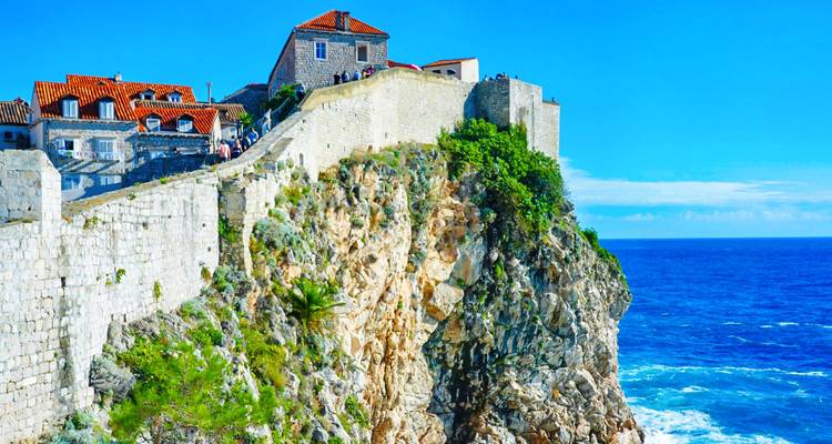 Stone ramparts of Dubrovnik’s city walls rise dramatically from a rugged cliff above the Adriatic.