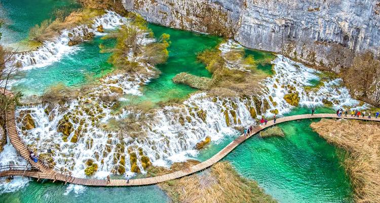 Boardwalk curves above cascading white falls and emerald pools viewed from above in Plitvice Lakes.