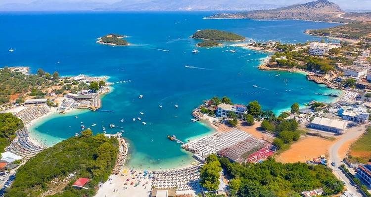 Luchtfoto van Ksamil's turquoise baaien bezaaid met kleine groene eilandjes en zandstranden.