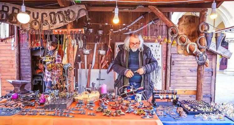 Traditional market stall in Krakow displaying handmade metal crafts with the artisan arranging his wares.