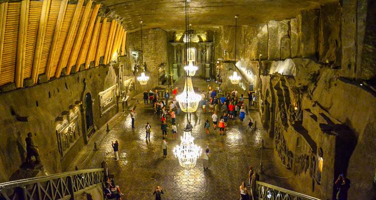 Visitors exploring an ornate underground chamber of the Wieliczka Salt Mine lit by chandeliers.