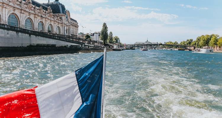 Vue depuis un bateau sur la Seine avec un drapeau français au premier plan.