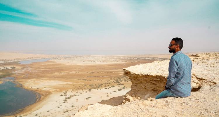 A man sitting on a cliff edge overlooking a desert landscape.