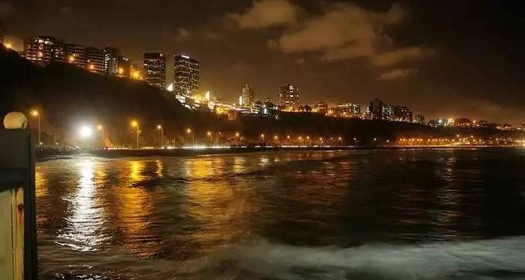 Nighttime view of Lima’s cliff-top skyline with streetlights reflecting across the dark ocean waters.