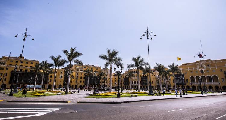 Colonial Plaza Mayor of Lima lined with yellow buildings and palm trees under a bright blue sky.