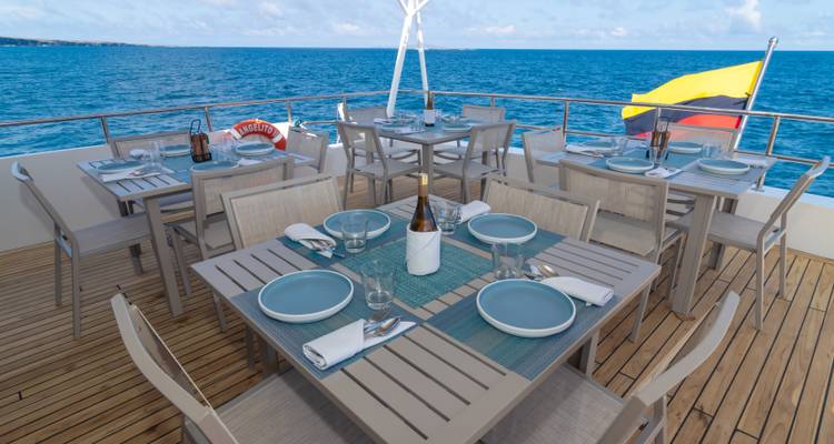 Stylish al-fresco dining area on a yacht deck set with champagne, plates and a vast blue ocean backdrop