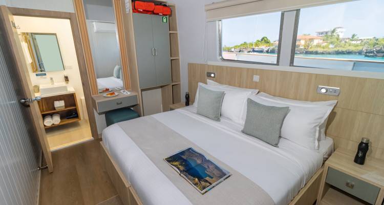 Bright yacht cabin featuring large bed, seaside window view and travel magazine on crisp linens