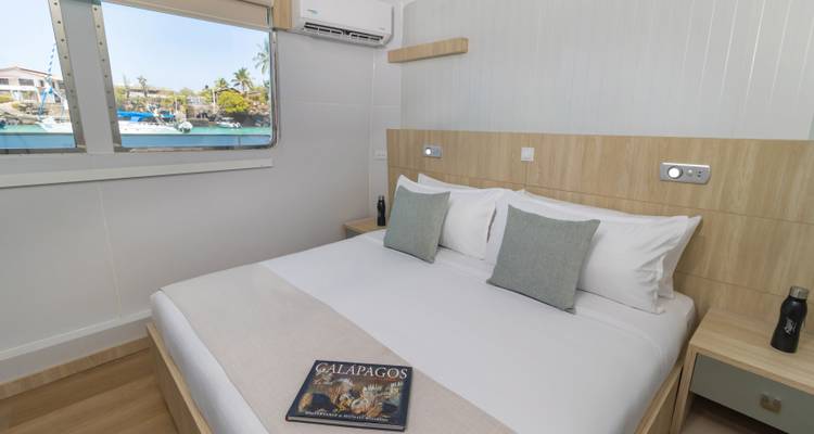 Modern yacht cabin with double bed, harbour view window and Galapagos book on the blanket
