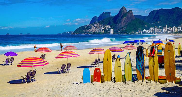 Paraguas coloridos, tablas de surf y tumbonas salpican una amplia playa de arena con oleaje turquesa, respaldada por los dramáticos picos de granito de Río.