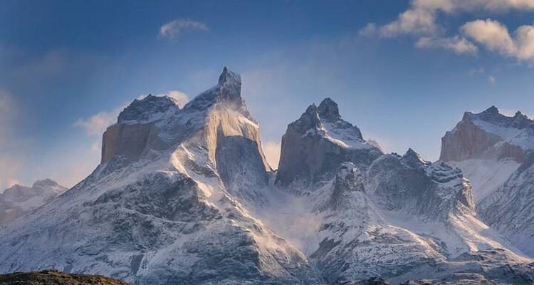Massif rocheux aux pics dentelés des Cuernos del Paine, saupoudré de neige, s'élevant de manière spectaculaire sous un ciel bleu