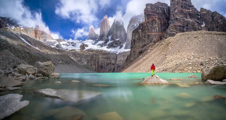 Randonneur solitaire sur un rocher surplombant un lac glaciaire turquoise et les imposantes aiguilles de granit des Torres del Paine