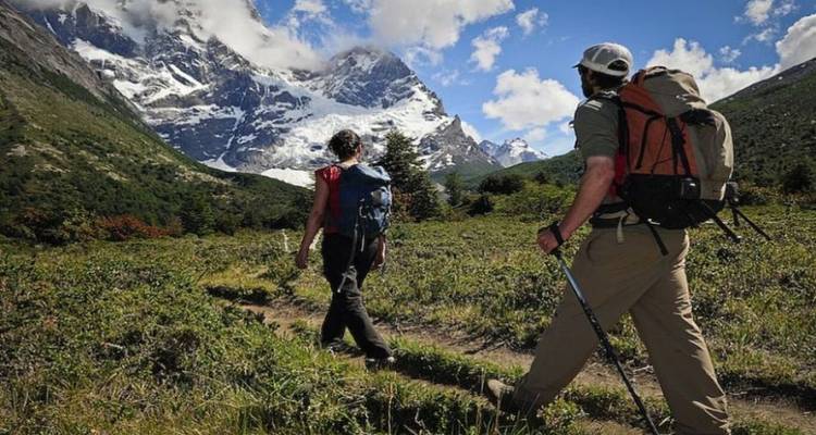 Deux randonneurs avec des sacs à dos marchant dans une prairie alpine en direction des pics enneigés en Patagonie