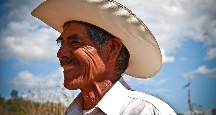 Portrait of a smiling elderly man wearing a traditional hat under a clear sky.