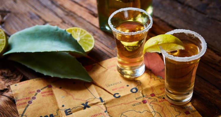 Close-up of tequila shots with lime slices on a textured surface.