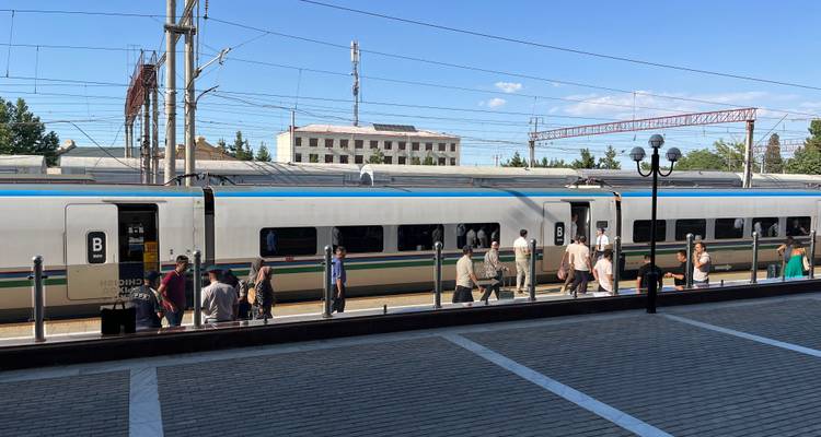 Passengers board a modern high-speed train at an Uzbek railway station on a sunny afternoon.