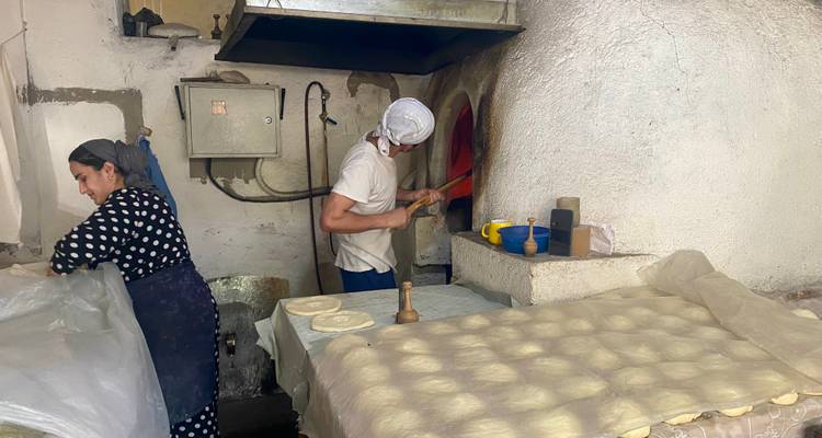 Local bakers prepare flatbread dough and tend a tandyr oven inside a rustic bakery.