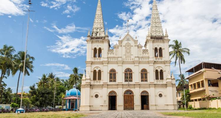 Wit kerkgebouw met twee torens, omringd door palmbomen.